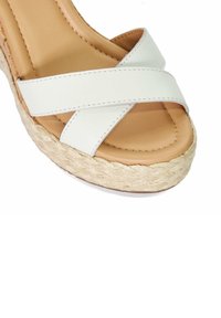 White cross-strap sandal featuring a woven jute platform sole and a tan cushioned footbed with visible stitching details.