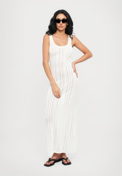 White, crocheted maxi dress featuring a scoop neckline and vertical stripe patterns. Paired with black flip-flops and sunglasses.