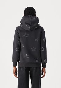 Sudadera gris oscuro con bordado de estrellas blancas. Presenta una capucha espaciosa, puños y dobladillo acanalados. La vista trasera muestra un patrón de estrellas dispersas.