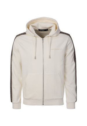 Kermanvärinen vetoketjullinen huppari, jossa on kiristysnauhat, etutaskut ja tummat kuvioidut raidat hihoissa, sekä hillitty logo-rintapainatus rinnassa.