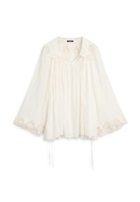 Camicia bianca larga con maniche ampie, dettagli in pizzo su polsini e collo e tessuto arricciato sotto lo scollo con laccetti.