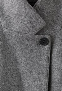 Manteau en laine gris avec un grand col et un seul bouton noir fermé près de la poitrine.