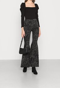 Body nero con maniche a sbuffo, abbinato a pantaloni neri a vita alta con un motivo floreale testurizzato. Accessoriato con una piccola borsa nera.