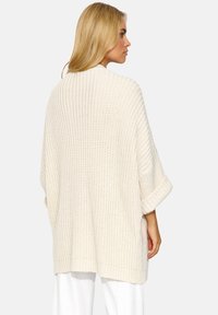 Sweter dziany w odcieniu łososiowym o luźnym kroju, z szerokimi rękawami i teksturowanym wzorem, prezentujący swobodny i przewiewny design.