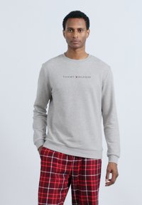 Sweatshirt din bumbac gri, cu guler rotund și un logo în centru. Asortat cu pantaloni de pijama în carouri roșii, cu accente albe.