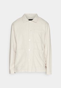 Beige knoopjacket gemaakt van lichte stof, met een puntige kraag, twee voorzakken en een enkele borstzak.