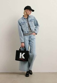 Šviesiai mėlynas džinsinis švarkas su dviem krūtinės kišenėmis, apsivilktas juodai baltu dryžuotu marškinėliu. Laisvi šviesiai mėlyni džinsai ir juodas totes krepšys su personažo dizainu.