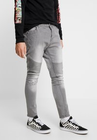 Jeans slim fit de un gris claro con textura acanalada en las rodillas y detalles desgastados, combinados con zapatillas a cuadros en blanco y negro.