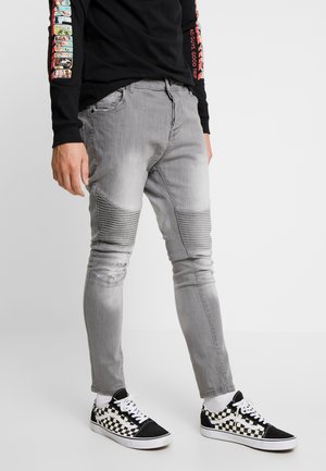 Jeans slim fit de un gris claro con textura acanalada en las rodillas y detalles desgastados, combinados con zapatillas a cuadros en blanco y negro.