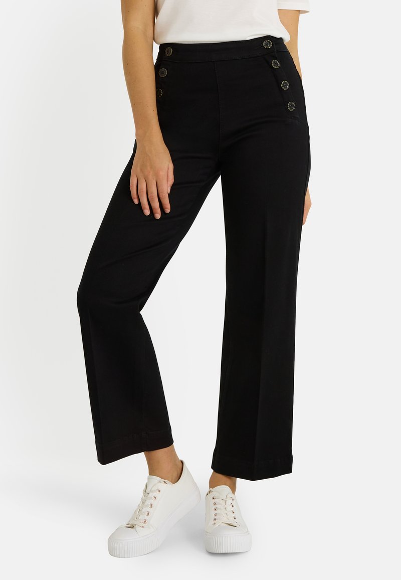 Pantalones negros de tiro alto con diseño de pierna ancha y cinco botones decorativos en el lado izquierdo. Combinados con zapatillas blancas.