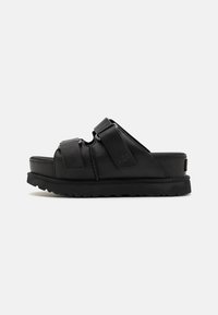 Sandales noires à glissière avec deux sangles réglables, semelle rembourrée et fond texturé. Fabriquées en matériau synthétique avec une marque UGG.
