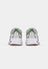 Chaussures de sport avec une semelle intermédiaire blanche et une semelle extérieure en caoutchouc marron, présentant un dessus gris clair avec des accents verts et des panneaux en mesh texturé.
