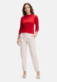 Maglietta rossa a maniche lunghe con collo tondo, abbinata a pantaloni beige chiaro sartoriali. La modella indossa sandali strappy bianchi. Tessuto morbido.