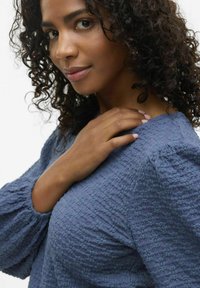 Blusa blu tessutata con maniche a sbuffo, caratterizzata da un motivo sottile, scollatura rotonda e vestibilità rilassata, che accentua la zona delle spalle.