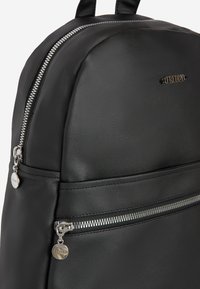 Zaino in pelle nera con una texture liscia, dotato di un compartimento principale con zip e di una tasca frontale con zip. Visibili finiture in metallo argentato.