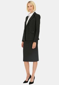 Czarna strukturalna marynarka z podwójnymi guzikami, połączona z czarną spódnicą ołówkową i czarnymi szpilkami zakończonymi w szpic. Biała koszula pod spodem.
