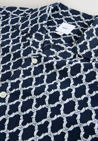 Cămașă navy cu mânecă scurtă, având un model geometric texturat alb, două butoane și o guler ascuțit. Eticheta spune "NEXT."