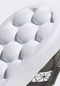 Semelle de chaussure présentant un rembourrage texturé blanc avec des formes arrondies et bulbeuses ; tige en cuir gris avec des détails accentués en blanc.