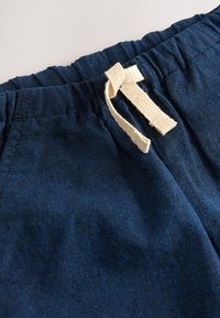 Mørkeblå stof med en blød tekstur og elastisk linning. Har en cremefarvet snøre til justering.