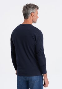 Musta pitkähihaisen paita, joka on valmistettu puuvillasta. Tässä paidassa on pyöreä kaula-aukko ja istuva muotoilu, joka näkyy takaa. Paidassa ei ole näkyviä logoja tai kuvioita.