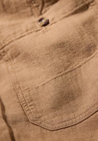 Tan tyg med fiskbensmönster har ett lockfack och en rund knapp. Texturen ser mjuk och något sliten ut.