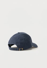 Μπλε μπλε καπέλο μπέιζμπολ με ρυθμιζόμενο ιμάντα και ορειχάλκινο πόρπη, εμφανίζεται από πίσω σε απλό φωτεινό φόντο.