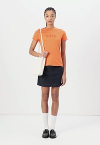 Orange cotton t-shirt with "BOSS" printed in matching tone, paired with a navy denim skirt, white knee-high socks, and black shoes.