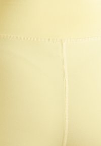 Mjuk och stretchig gul tygmidjeband med slät textur, utrustad med en central söm och subtila sömnaddetaljer, designad för komfort och passform.