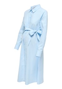 Φόρεμα εγκυμοσύνης σε ανοιχτό μπλε με μακριά μανίκια, μπροστινά κουμπιά και ζώνη με φιόγκο δεμένη πάνω από την κοιλιά.