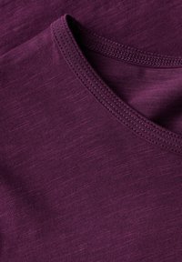 Tessuto viola con una finitura testurizzata. Il collo presenta un bordo a costine, che mette in risalto il materiale morbido e elastico.
