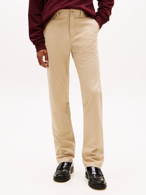 Chinos bege com um design de perna reta, feitos de tecido de algodão. Combinam com sapatos slip-on pretos brilhantes e um sweatshirt bordô.