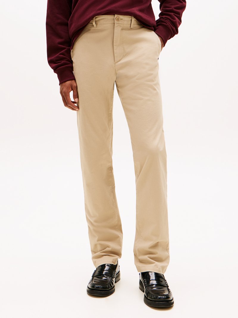 Chinos bege com um design de perna reta, feitos de tecido de algodão. Combinam com sapatos slip-on pretos brilhantes e um sweatshirt bordô.