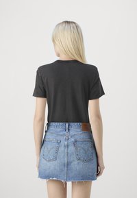 Zwarte katoenen t-shirt met korte mouwen, gecombineerd met een blauwe denim minirok met een rafelrand en een leren label achteraan.