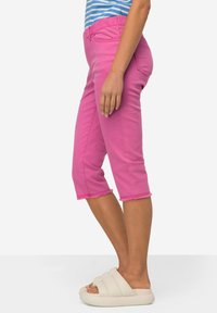 Pantaloni capri rosa con orlo a frange, dotati di vita elasticizzata e vestibilità aderente, abbinati a sandali bianchi con suola piatta.