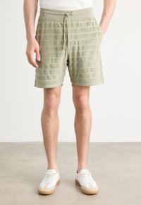 Lichtgroene badstof shorts met een horizontale gestreepte structuur, elastische tailleband en trekkoord. Gecombineerd met witte sneakers.