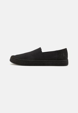 Chaussures noires à enfiler avec une tige en toile, semelle en jute texturé et logo subtil sur le talon. Design simple, sans fermetures visibles.
