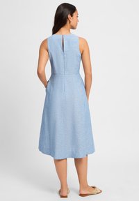 Lichtblauwe mouwloze jurk met een openrugdetails, ontspannen silhouet en een lengte tot de knie. Gemaakt van textuurstof met een subtiel patroon.