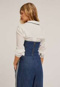 Denimkorsett med en strukturerad design, med en diskret dragkedja bak och i kombination med en vit skjorta med uppvikta ärmar.