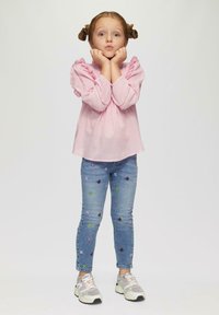 Hele roosa pluus pitsiliste varrukatega, sinised teksased, millel on värvilised liblikamustrid, ja hallid tossud roosade aktsentidega.