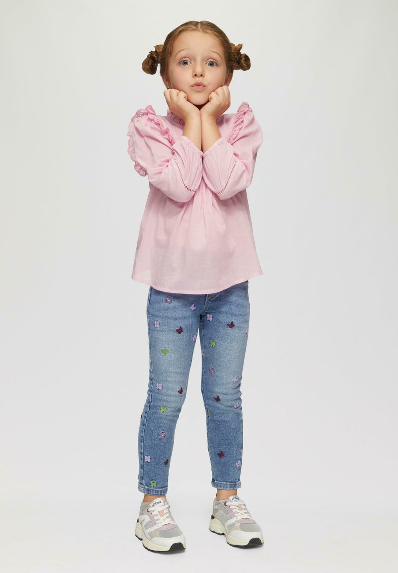 Hele roosa pluus pitsiliste varrukatega, sinised teksased, millel on värvilised liblikamustrid, ja hallid tossud roosade aktsentidega.