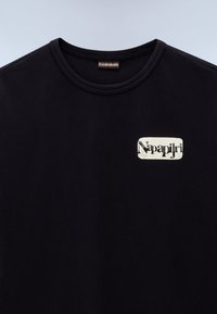 Musta puuvillapaita, jossa on pyöreä pääntie ja suorakulmainen kerma-logo, jossa lukee "Napapijri" mustalla tekstillä.