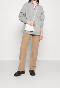 Grå zip-up sweatshirt, beige kordfluwelbyxor och svarta platåstövlar. Modellen håller en liten vit crossbody-väska.