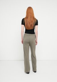 Wide-leg trousers in olive green fabric with a stretch waistband, paired with a black fitted top, viewed from the back.