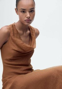 Brown, sleeveless dress with a cowl neckline, made of textured fabric. The design features a relaxed fit and smooth draping.