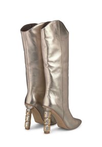 Bottes métalliques dorées arrivant jusqu'au genou avec un ajustement serré et un bout pointu, dotées d'un talon bloc orné d'accents en acrylique transparent.