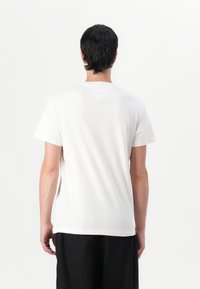 White cotton T-shirt with a crew neck, short sleeves, and a relaxed fit. Features a decorative back yoke seam detail.