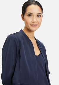 Blouse légère bleu marine avec un col châle et une ouverture à l'avant. Texture lisse et design simple, présentant un aspect superposé.