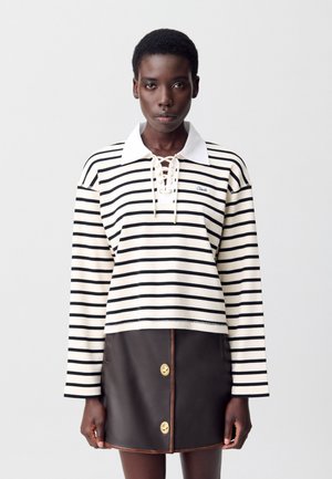 Top à manches longues rayé en crème et noir, avec un col blanc et un détail à lacets. Associé à une jupe en cuir marron avec des boutons dorés.