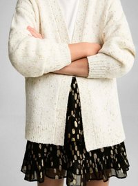 Crème gebreide cardigan met een losse pasvorm, voorzien van geribde manchetten, gecombineerd met een zwarte, gelaagde rok met gouden stippen.