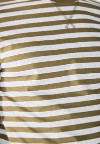 Olive and white striped cotton shirt with a v-neckline. Stitches in a contrasting color form an 'X' pattern at the neckline.